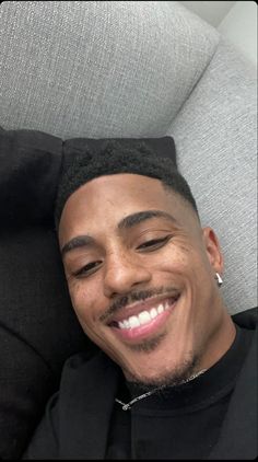 a man smiling while laying down on a gray couch with his head turned to the side