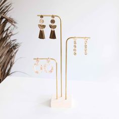 three pairs of earrings are on display in front of a white wall and palm tree