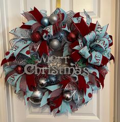 a christmas wreath is hanging on the front door with ornaments around it and merry lettering