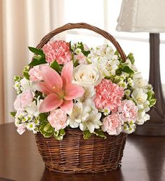 a basket filled with pink and white flowers on top of a wooden table next to a lamp