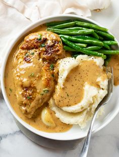 a white bowl filled with mashed potatoes and gravy next to green beans