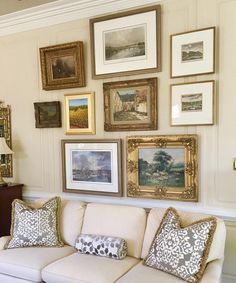 a living room filled with lots of framed pictures on the wall above a white couch