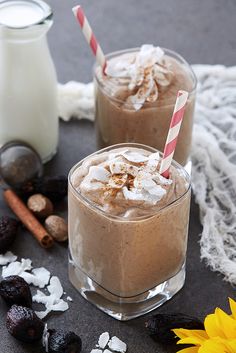 two glasses filled with chocolate milkshakes on top of a table next to nuts