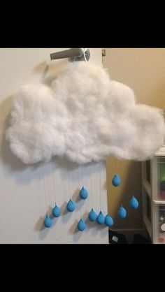 a white cloud with blue raindrops hanging from it's side on a wall