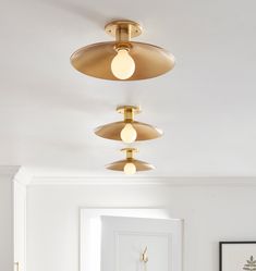 three lights are hanging from the ceiling in this white and gold room with an open door