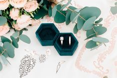 two wedding rings are sitting in their velvet boxes next to some flowers and greenery