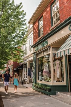 two people walking down the street in front of shops with green awnings and brick buildings