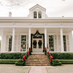 a white house decorated for christmas with wreaths and decorations on the front door steps