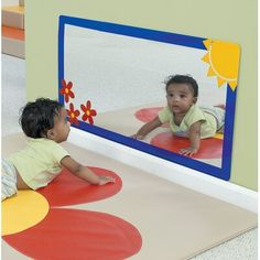 two small children sitting on the ground in front of a mirror