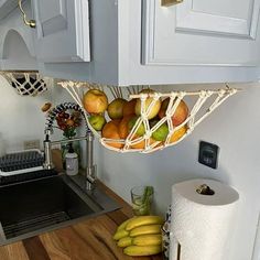 some fruit is in a basket hanging from the wall above a kitchen sink and counter