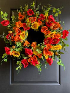 an orange and red wreath on a door with greenery in the center is surrounded by flowers