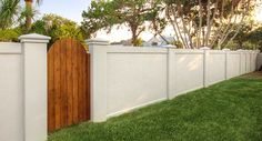 a white fence with a wooden gate in front of some palm trees and green grass