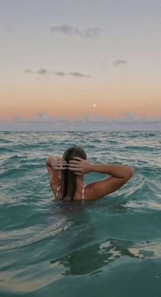 a woman in the ocean with her back to the camera, covering her face and head