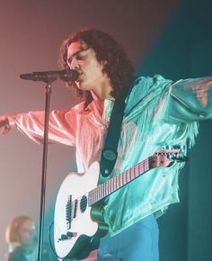 a man holding a white guitar while standing in front of a microphone