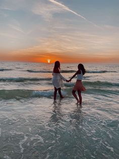 two girls are holding hands while walking in the water at sunset or sunrise on the beach