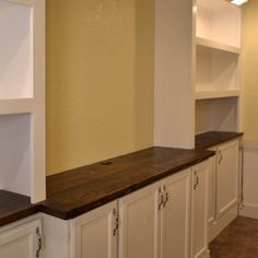 an empty kitchen with white cabinets and wood counter tops on the wall, along with brown tile flooring