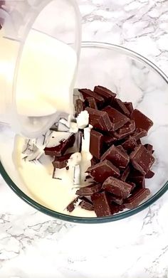 someone pouring milk into a bowl filled with chocolate and marshmallows on a marble counter top