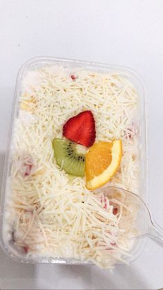 a plastic container filled with cheese and fruit on top of a white table next to a spoon