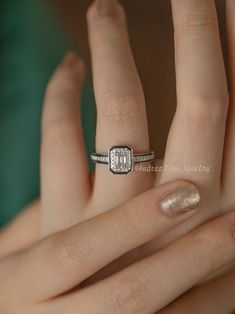 a woman's hand with a diamond ring on top of her finger and the other hand holding an engagement ring