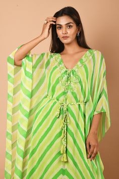 Lime green kaftan tunic with all-over Leheriya print, embroidered neckline and criss-cross tie-up. Comes with braided belt.
Component: 2
Printed, Embroidered
Neckline: V-Neck
Sleeve Length: Asymmetric
Fabric: Georgette
Color: Green
Asymmetric hem
Braided belt with tassels
Note: The inner slip worn by the model is not for sale - Aza Fashions Traditional Green V-neck Tunic, Green Bohemian Kaftan For Festive Occasions, Green Tunic Kaftan For Festive Occasions, Green V-neck Kaftan For Beachwear, Green Bohemian Tunic For Festive Occasions, Festive Green Kurta For Beach Occasions, Green Maxi Length Kaftan For Spring, Bohemian Green Festive Tunic, Festive Green Bohemian Tunic