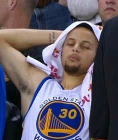 a basketball player sleeping in the stands with his head covered by a towel as fans look on