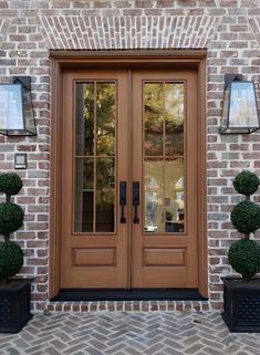 two potted topiary plants in front of a brick building with double doors and sidelights