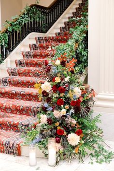 a staircase decorated with flowers and greenery next to candles on the floor in front of some stairs