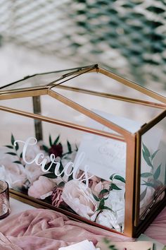 a glass box filled with flowers on top of a pink cloth covered table next to a candle