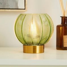 a green vase sitting on top of a table next to a brown bottle with reeds in it