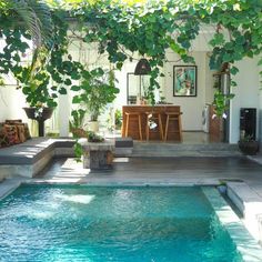 a small pool in the middle of a patio with chairs and tables around it, surrounded by greenery