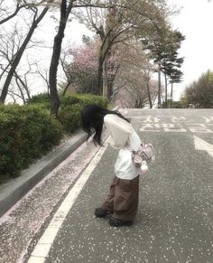 a woman standing on the side of a road next to a tree filled with pink flowers