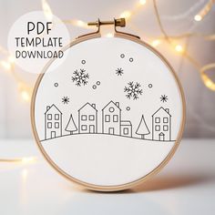 an embroidery pattern with houses and snowflakes on it, in front of a christmas tree