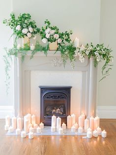 a fireplace with candles and flowers on it in front of a fire place filled with greenery