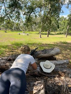 a woman kneeling down next to a tree trunk with a hat on top of it