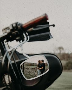 an image of a man and woman kissing in the reflection of a motorcycle's side mirror