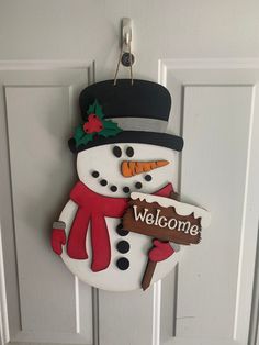 a snowman holding a welcome sign hanging from the front door with a hat and scarf on