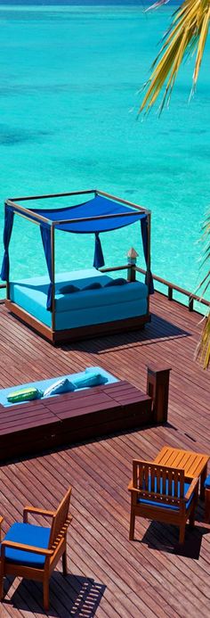 a bed sitting on top of a wooden deck next to the ocean with blue water