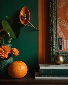 an orange sits on a table next to a vase with flowers in it and two books