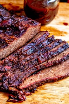 sliced meat sitting on top of a cutting board next to a jar of bbq sauce