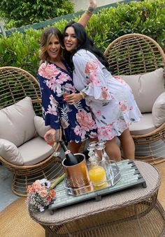 two women standing next to each other in front of some wicker chairs and drinks