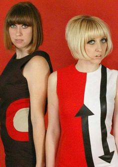 two women standing next to each other in front of a red wall