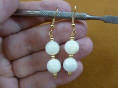 (Internal #EE-473-14) This is a beautiful pair of white mother of pearl (from the South Seas), two 10mm round bead, beaded dangle earrings with three 3mm gold alloy textured bead accents, on gold tone alloy hypoallergenic french wires.   This is a nice pair of earrings, great for a classic look.This is the exact pair you will receive.WE SHIP WORLDWIDE! Other accepted payment: Credit card (Mastercard/Visa/Discover) inquire for details. White Wire Wrapped Round Bead Earrings, White Wire Wrapped Round Pearl Earrings, Adjustable White Pearl Earrings With Round Beads, Nice Jewelry, Gold Alloys, French Wire, South Seas, Pearl Gemstone, Beaded Dangle Earrings