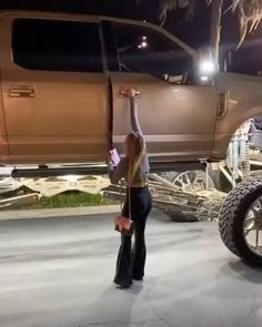 a woman standing in front of a truck with her hand up to the sky above it