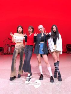 four girls standing in front of a red wall with their hands up to the side