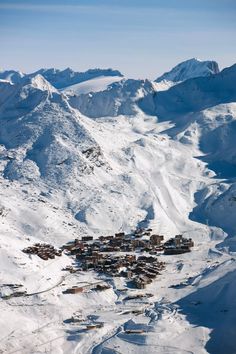 an aerial view of a ski resort surrounded by snow covered mountains in the distance are houses and buildings