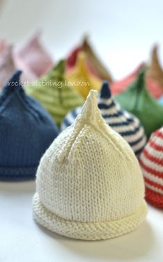 several knitted baby hats lined up on a table with the top one folded down