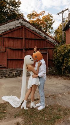 a man and woman are kissing in front of a house with an orange mask on their face