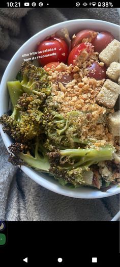 a bowl filled with broccoli, tomatoes and croutons on top of a blanket