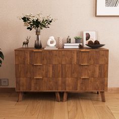 a wooden dresser sitting next to a plant and pictures on top of the drawers in a room