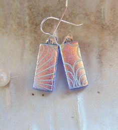 "The stones in these beautiful earrings measure approximately 13/16\" by less than 3/8\".  They are hung with sterling silver French wire hooks and hang approximately 1 1/4\".  The pattern on these earrings were sand blasted onto the glass, and then coated with dichroic.  When fired and left un-capped with clear, it leaves a beautiful satin and shiny textured dichroic service.  The base glass in these earrings is transparent blue with peach-gold colored dichroic on top.   Thank you for looking in my shop.  All of my pendants and earrings will arrive in a gift box.  I do my best to accurately photograph my work so you will be happy with your purchase. Dichroic Glass changes colors with different lighting and different angles, therefore making it difficult to photograph. You must see my dich Nickel Free Long Drop Blue Earrings, Blue Sterling Silver Earrings With French Hook, Blue Dangle Earrings With French Hook, Fusion Dual-tone Metal Jewelry, Fusion Style Multi-stone Teardrop Earrings, Multicolor Soldered Dangle Earrings, Sterling Silver Blue French Hook Earrings, Nickel-free Long Drop Blue Earrings, Multicolor Nickel-free Dangle Teardrop Earrings